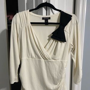 Elegant cream colored top with a black bow and decorative buttons on the sleeve